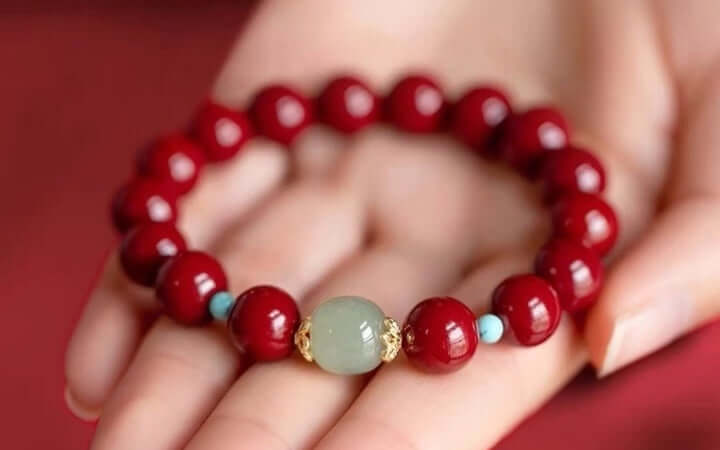 Hand holding a red feng shui bracelet with green bead for energy and balance activation.