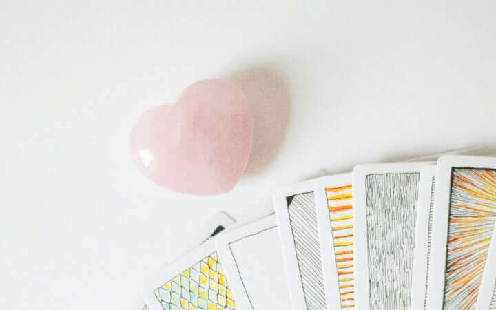 Heart-shaped rose quartz on white background with tarot cards implying emotional healing benefits.