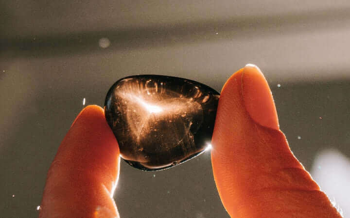 Hands holding a polished obsidian stone reflecting light, highlighting its deep color and energy.